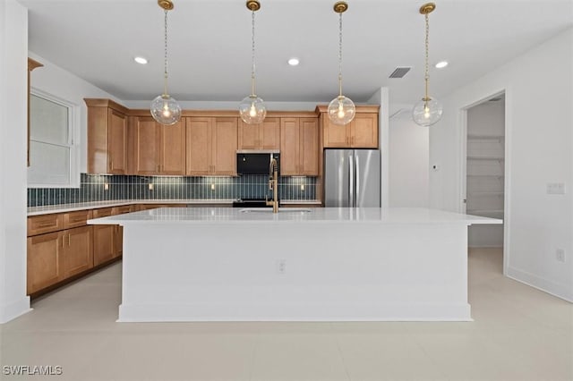 kitchen with visible vents, light countertops, freestanding refrigerator, a center island with sink, and backsplash