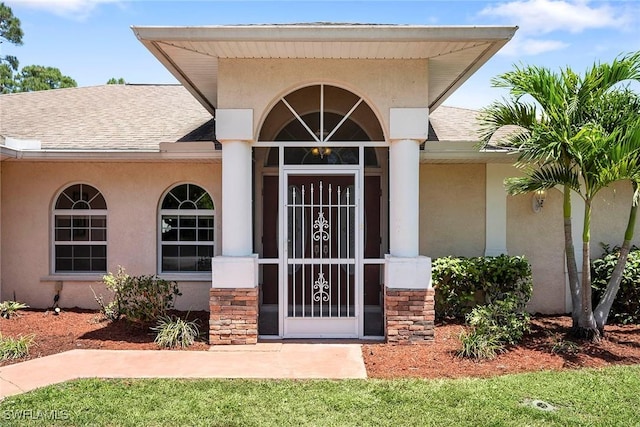 view of exterior entry with stucco siding, a shingled roof, and stone siding