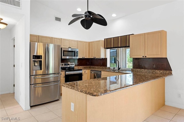 kitchen with a sink, stainless steel appliances, dark stone countertops, light brown cabinetry, and visible vents