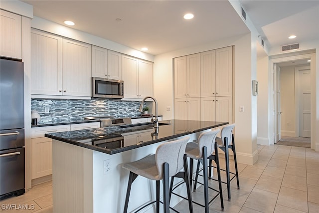 kitchen featuring decorative backsplash, appliances with stainless steel finishes, visible vents, light tile patterned flooring, and a kitchen bar