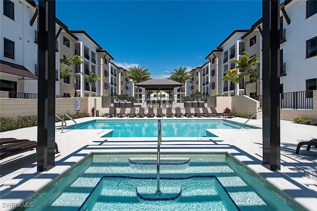 pool with a patio, fence, a community hot tub, and a residential view