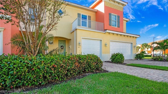 view of front of house with a balcony, a tile roof, decorative driveway, an attached garage, and stucco siding