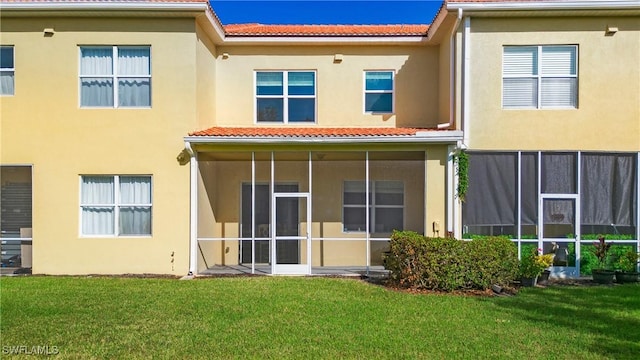 back of house featuring a lawn, a sunroom, stucco siding, and a tiled roof