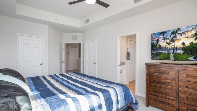 bedroom featuring light colored carpet, visible vents, a raised ceiling, and ensuite bath