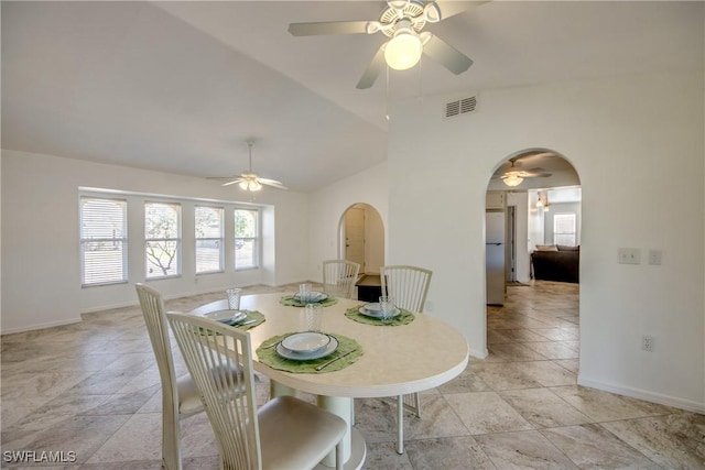 dining space with arched walkways, ceiling fan, baseboards, and vaulted ceiling