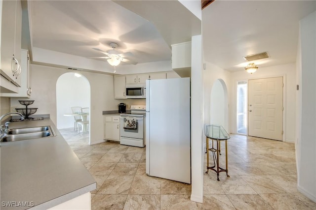 kitchen featuring white appliances, a sink, arched walkways, ceiling fan, and baseboards