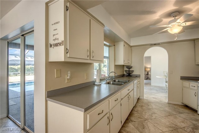 kitchen with a sink, arched walkways, a ceiling fan, baseboards, and white cabinetry