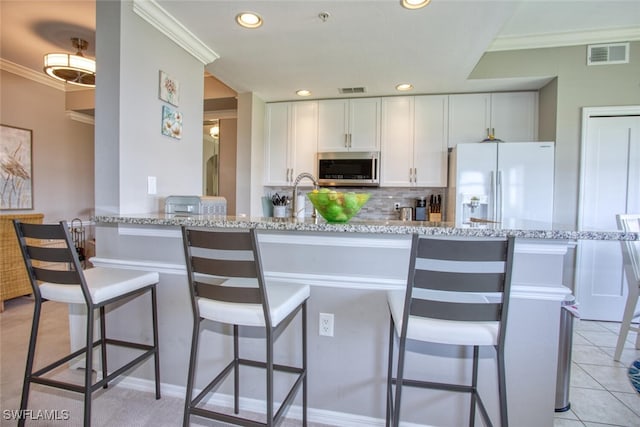 kitchen featuring decorative backsplash, visible vents, white refrigerator with ice dispenser, white cabinets, and stainless steel microwave
