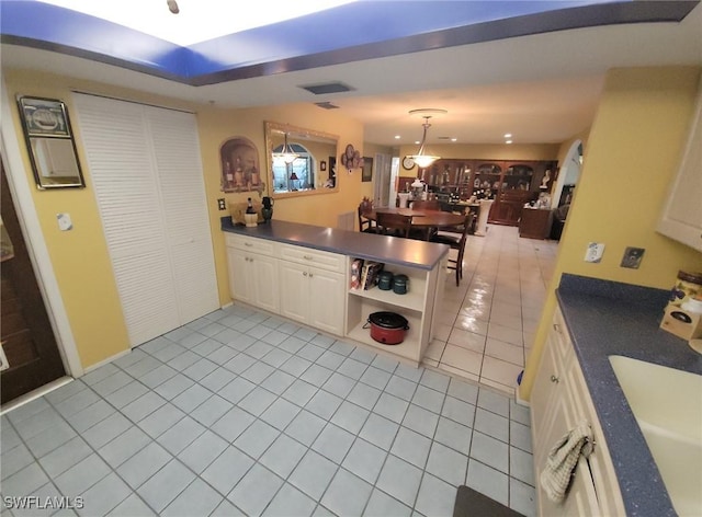 kitchen with a sink, light tile patterned flooring, a peninsula, dark countertops, and white cabinets