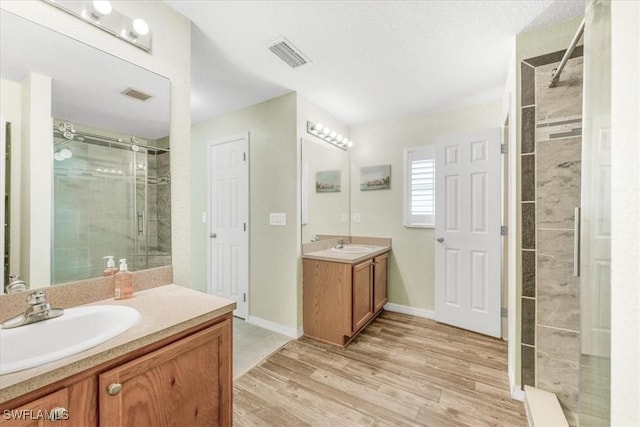 3210 31st St W, Lehigh Acres, FL 33971 - full bathroom featuring visible vents, a stall shower, wood finished floors, two vanities, and a sink