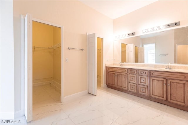 bathroom featuring marble finish floor, a sink, double vanity, and baseboards