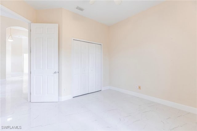 unfurnished bedroom with a closet, marble finish floor, visible vents, baseboards, and arched walkways