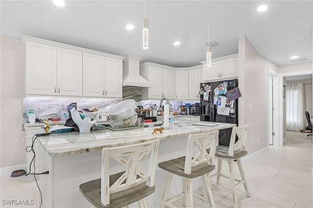 kitchen with baseboards, a kitchen bar, black refrigerator with ice dispenser, custom exhaust hood, and backsplash