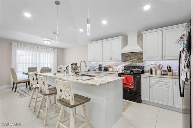 kitchen with a sink, custom range hood, backsplash, black electric range, and white cabinets