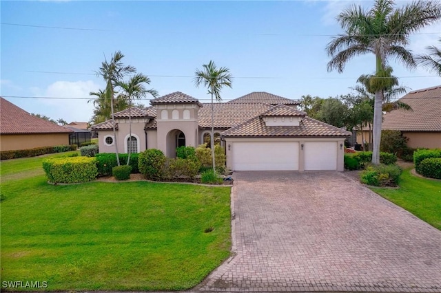 mediterranean / spanish home with a tiled roof, decorative driveway, stucco siding, a front lawn, and a garage