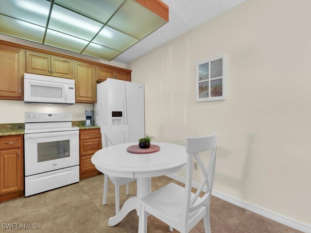 kitchen featuring light tile patterned floors, brown cabinets, white appliances, and light stone countertops