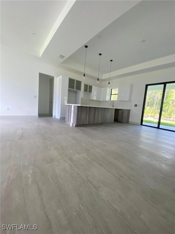 unfurnished living room with visible vents, a tray ceiling, and a high ceiling