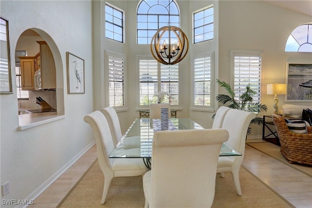 dining area featuring a high ceiling, a chandelier, baseboards, and light wood finished floors