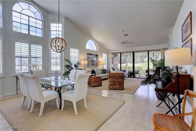 dining room with high vaulted ceiling, ceiling fan with notable chandelier, wood finished floors, and visible vents