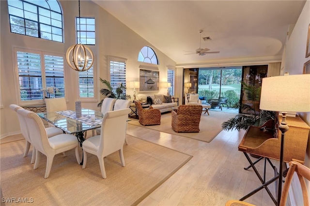 dining space with visible vents, light wood-style flooring, ceiling fan with notable chandelier, and high vaulted ceiling