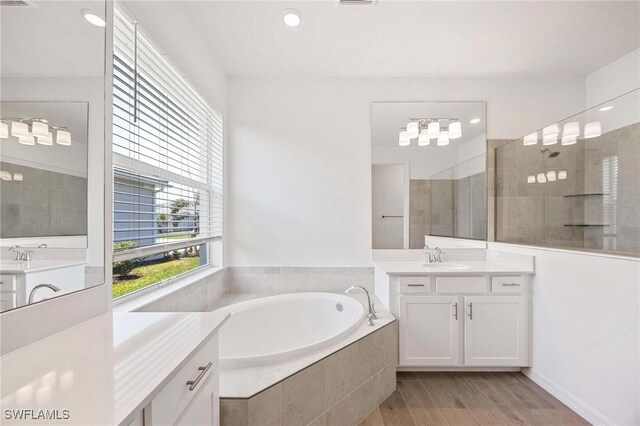 bathroom featuring a garden tub, wood finished floors, a walk in shower, two vanities, and a sink