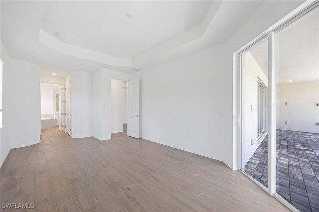 unfurnished bedroom with connected bathroom, a tray ceiling, baseboards, and wood finished floors
