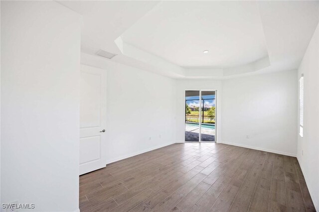 spare room with baseboards, a tray ceiling, and wood finished floors