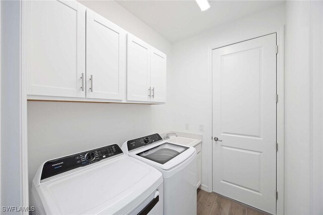 laundry room with a sink, cabinet space, independent washer and dryer, and wood finished floors