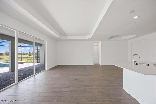 unfurnished living room with wood finished floors, a sink, baseboards, a tray ceiling, and recessed lighting
