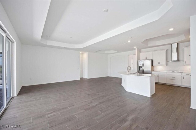 kitchen featuring stainless steel fridge, open floor plan, a raised ceiling, and wall chimney exhaust hood