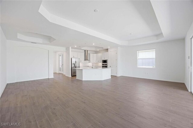 unfurnished living room with baseboards, a sink, a raised ceiling, and wood finished floors