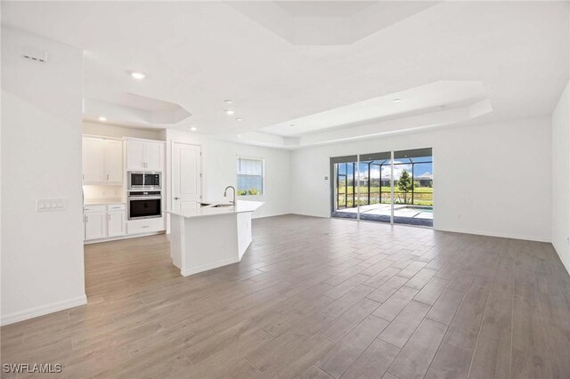 unfurnished living room with a sink, a raised ceiling, and light wood-type flooring