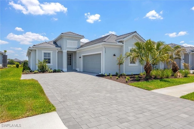 view of front of property featuring a garage, a front yard, decorative driveway, stucco siding, and a tiled roof
