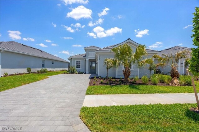 view of front of house featuring decorative driveway, stucco siding, a tile roof, and a front yard