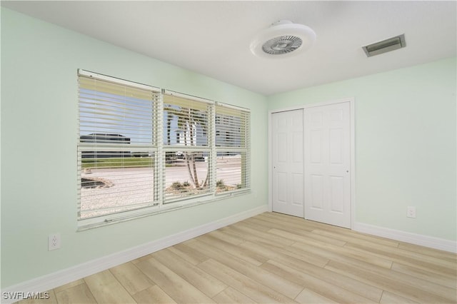 unfurnished bedroom with a closet, visible vents, wood finished floors, and baseboards