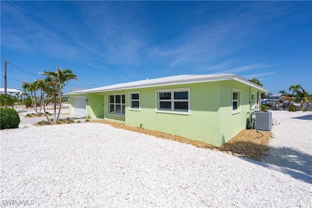 back of house featuring driveway, central AC, an attached garage, and stucco siding