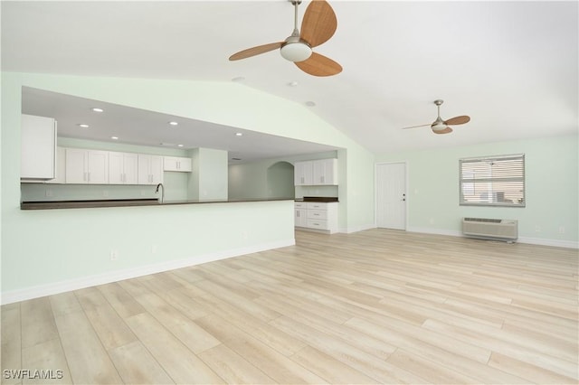 unfurnished living room with a wall unit AC, a ceiling fan, light wood-style flooring, and vaulted ceiling
