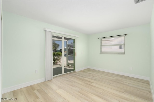 empty room with baseboards, visible vents, wood finished floors, and a healthy amount of sunlight