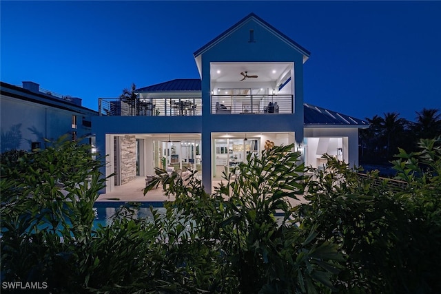 1380 Pelican Ave, Naples, FL 34102 - back of house at twilight with a balcony, a standing seam roof, a patio area, metal roof, and stucco siding