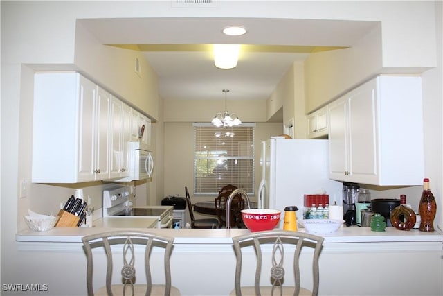 kitchen with white appliances, decorative light fixtures, light countertops, white cabinets, and a notable chandelier