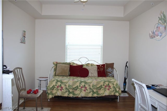 bedroom with baseboards, wood finished floors, and a tray ceiling