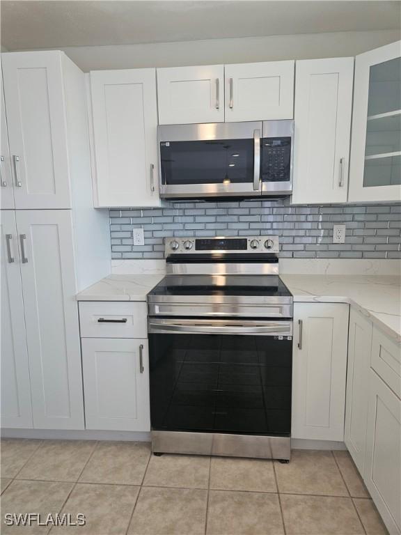 kitchen featuring glass insert cabinets, white cabinetry, tasteful backsplash, light stone counters, and appliances with stainless steel finishes