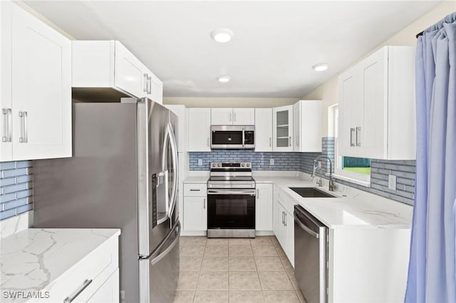 kitchen with light stone countertops, appliances with stainless steel finishes, decorative backsplash, and a sink