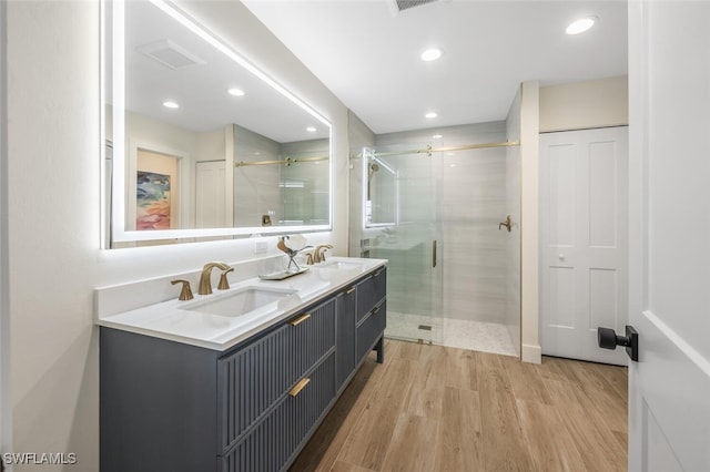 full bath featuring double vanity, a stall shower, wood finished floors, a sink, and recessed lighting