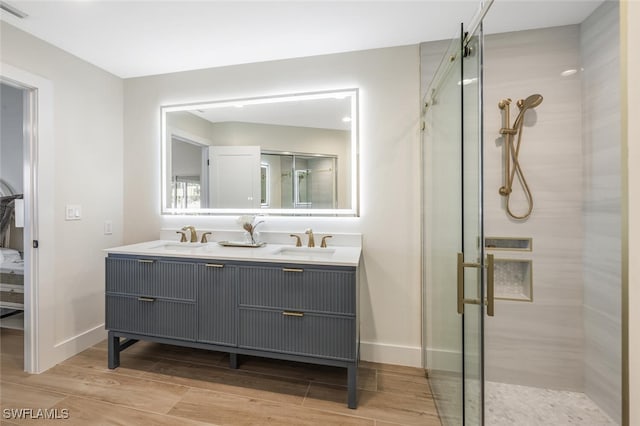 ensuite bathroom featuring double vanity, a stall shower, a sink, and wood finished floors