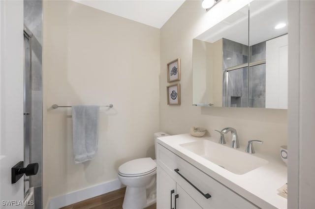 bathroom with vanity, toilet, baseboards, wood finished floors, and a stall shower