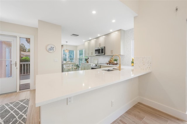 kitchen with a peninsula, light wood-style floors, light countertops, a sink, and stainless steel appliances