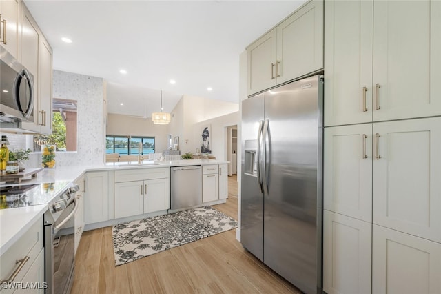 kitchen featuring light wood-type flooring, a sink, light countertops, a peninsula, and stainless steel appliances