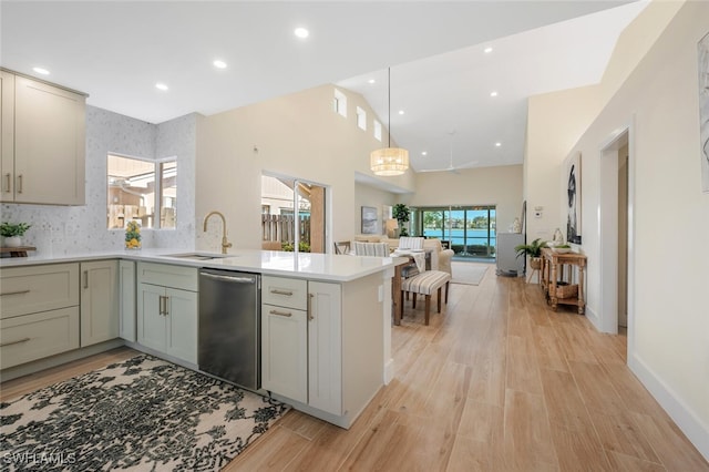 kitchen featuring a sink, light countertops, a peninsula, open floor plan, and stainless steel dishwasher