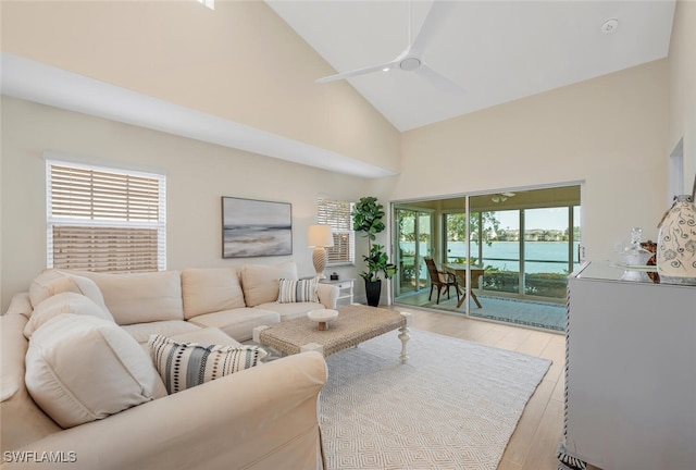living area with a water view, a ceiling fan, high vaulted ceiling, and light wood finished floors